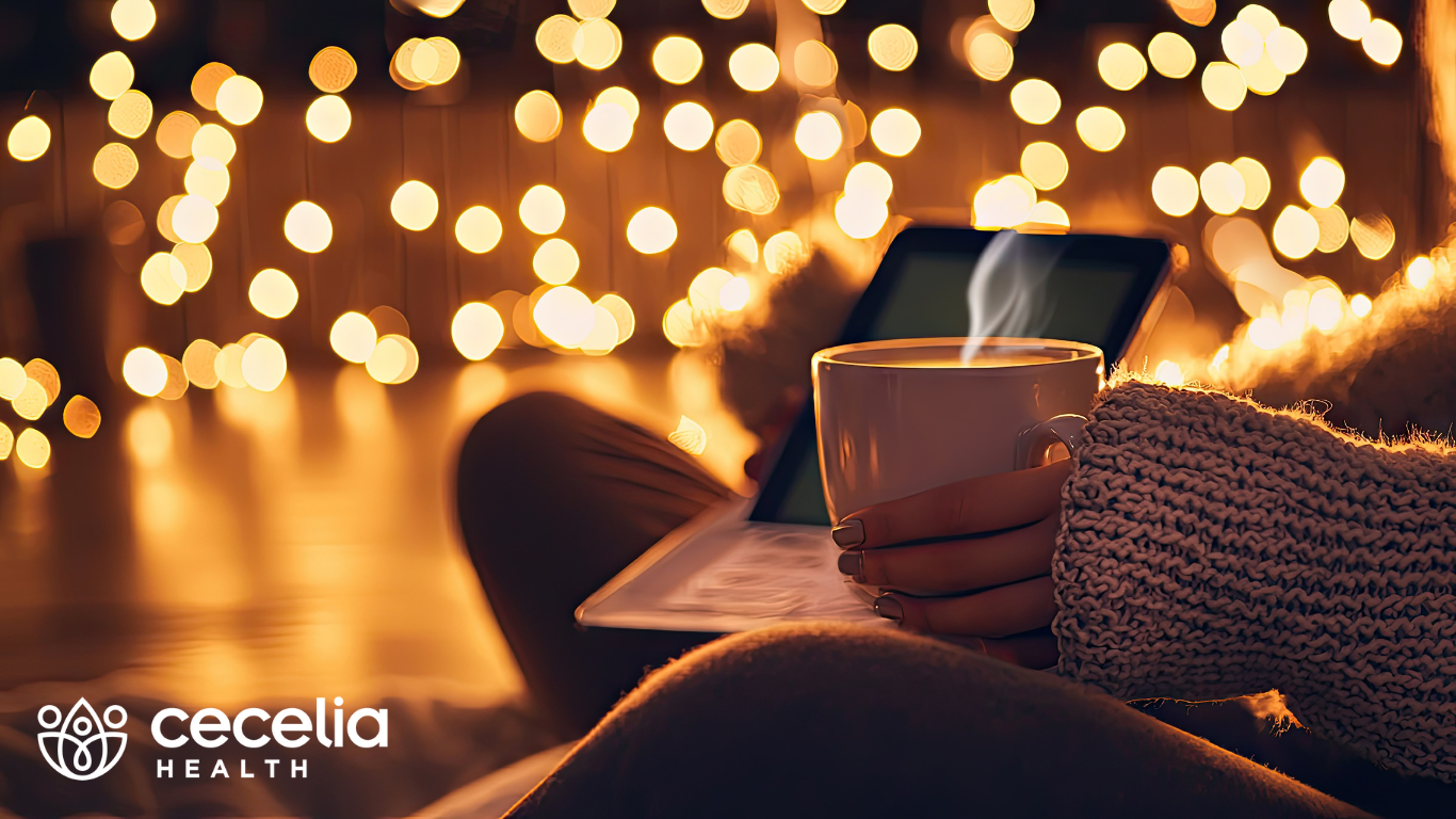 woman drinking out of a warm mug with christmas lights in the background