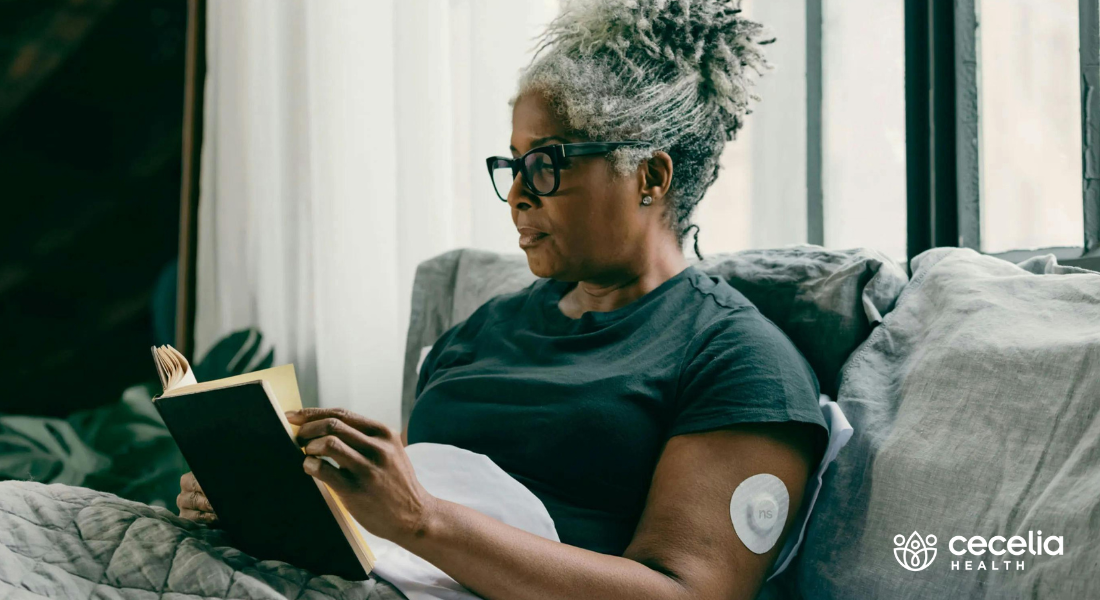 woman sitting in bed reading book wearing CGM