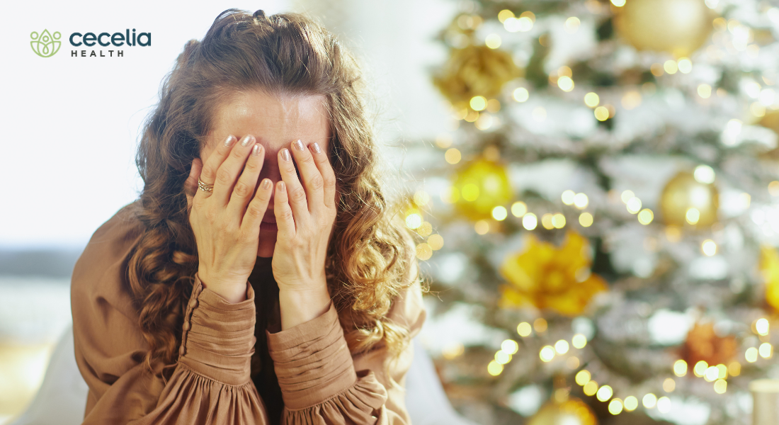 woman sitting in front of christmas tree with hands in front of her face stressed