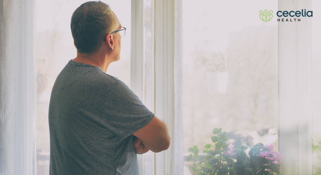 man standing and looking out window arms crossed