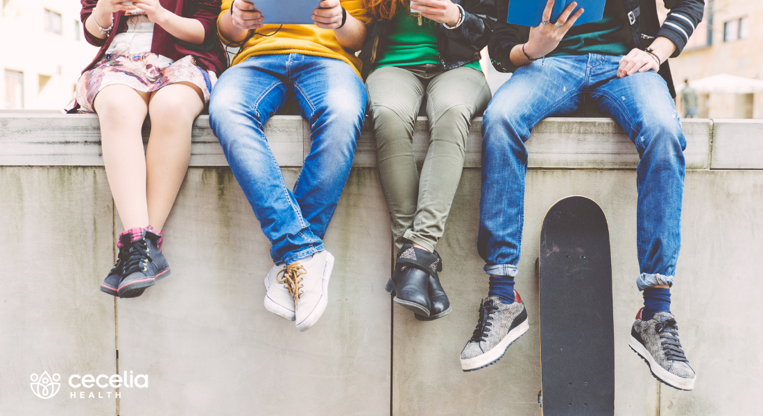 teenagers sitting on a concrete wall looking at phones and reading books